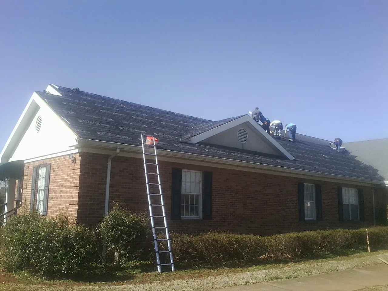Crew tearing shingles off a brick ranch roof with a ladder set — Metal Roof Repair work by our crew in Arnold
