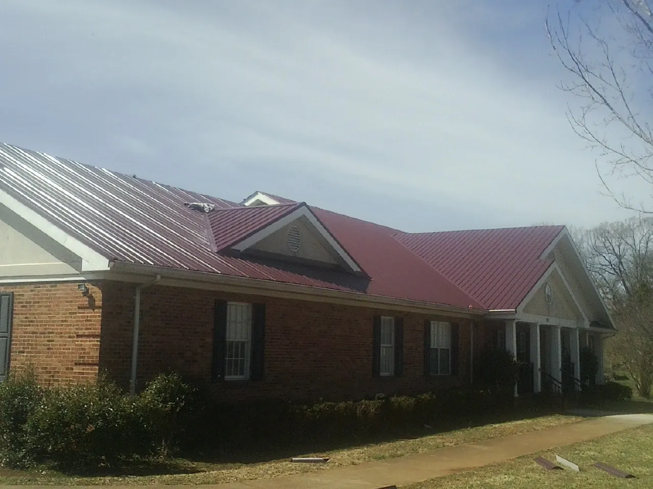 Red metal roof with gabled entries on a long brick building, from a Hail Damage Roof Repair job in Arnold