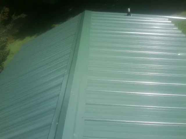 New green metal panels meeting at the ridge of a roof — Flat Roof Repair work by our crew in Arnold