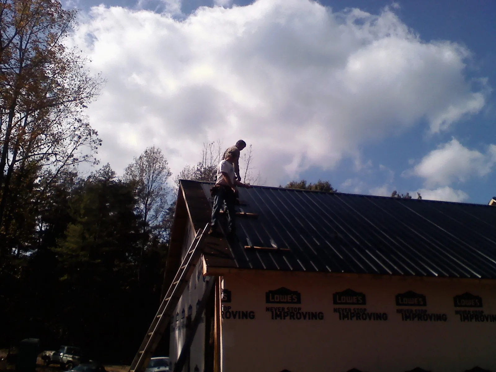 Roofer fastening dark metal panels high against a cloudy sky, from a Roof Inspection job in Arnold